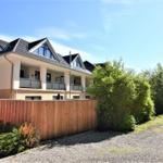 Modernes Haus mit Balkonen und Holzzaun. Grünflächen und klarer Himmel.