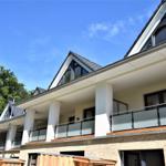 Moderne Villa mit Balkon und Dachfenstern, umgeben von Bäumen unter blauem Himmel.