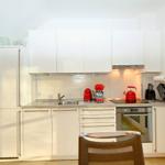 Moderne Küche mit weißen Schränken, roten Küchenutensilien und integriertem Ofen.