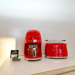 Auf der Arbeitsfläche stehen zwei rote Küchengeräte und ein kleines digitales Gerät.