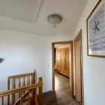 Flur mit Holzgeländer, Wandbild und Blick in Schlafzimmer mit Kleiderschrank.