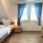 Schlafzimmer mit Holzbett, Nachttisch und Kleiderschrank. Fenster mit blauen Vorhängen.