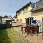 Haus mit Terrasse, Garten und Strandkorb. Tisch und Stühle stehen draußen.