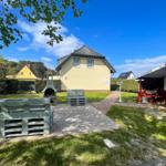 Haus mit Garten, Grill und Holzbank unter blauem Himmel.