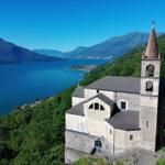 Alte Kirche mit Turm auf Hügel über See. Berglandschaft und Wasser im Hintergrund.