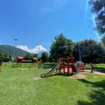 Großer Spielplatz mit Rutschen und Klettergerüsten auf grünem Rasen vor Berglandschaft.