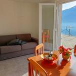 Wohn- und Essbereich mit Blick auf See und Berge. Holztisch, Sofa und Terrasse.