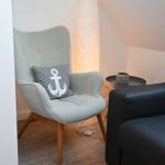 Ein grauer Sessel mit Kissen und eine schwarze Couch stehen in einem Raum mit Holzboden.