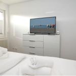 Schlafzimmer mit weißem Bett, Fernseher und Fenster mit Jalousie.