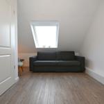 Ein Raum mit grauem Sofa, Holzboden und Dachfenster. An der Wand hängt ein Bild.