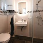 Badezimmer mit Dusche, Waschbecken und Toilette. Fliesen und Spiegel sichtbar.