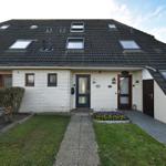 Einfamilienhaus mit Dachgauben, weißen Wänden und Vorgarten mit Blumenbeet.