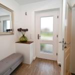 Eingangsbereich mit Spiegel, Sitzbank und Tür. Nebenraum ist Bad mit Toilette.