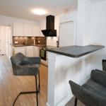 Küche mit Essbereich, grauen Barhockern und Holzboden.