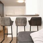 Barhocker vor einer Küchenzeile mit Tresen. Im Hintergrund Treppe und Wohnbereich.