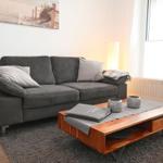 Ein grauer Sofa mit Kissen steht vor einem Fenster. Davor befindet sich ein Holztisch.