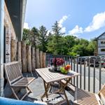 Terrasse mit Holztisch und Stühlen, Blick auf grüne Bäume und benachbarte Gebäude.
