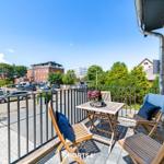Terrasse mit Holztisch und Stühlen, Blick auf Parkplatz und Gebäude.