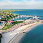 Hafen mit Yachten, Strand und Windkraftanlagen im Hintergrund.