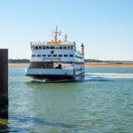 Fährschiff Nordfriesland fährt durch ruhiges Wasser, umgeben von Vögeln und Holzpfählen.