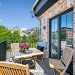 Terrasse mit Holztisch und Stühlen, Blick auf Grünflächen und Gebäude.