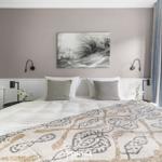 Schlafzimmer mit Bett, Wandbild und Fenster. Helle Einrichtung mit grauen und weißen Akzenten.