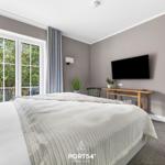 Schlafzimmer mit Bett, TV und Balkon mit Blick auf Bäume.