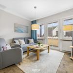 Wohnzimmer mit Sofa, Sessel, Couchtisch und TV. Terrasse über Schiebetür.