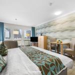 Schlafzimmer mit Bett, Sofa, TV und Esstisch. Wandtapete und Holzmöbel.