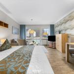 Schlafzimmer mit Bett, Sofa, Fernseher und Esstisch. Wand mit Muster, Fenster mit Blick.