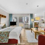 Schlafzimmer mit Bett, Wohnbereich mit Sofa und Küchenzeile. Balkon mit Blick auf Dächer.