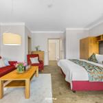 Ein Schlafzimmer mit rotem Sofa, Holztisch und Bett mit Muster.