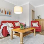 Ein Wohnzimmer mit rotem Sofa, Holztisch und Wandbild mit Segelbooten.