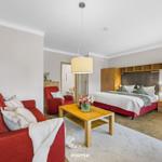 Wohn- und Schlafbereich mit rotem Sofa, Holztisch und Bett mit Holzgestell.