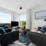 Wohnzimmer mit schwarzen Ledermöbeln, großen Fenstern und Blick aufs Meer.