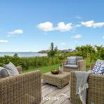 Terrasse mit Rattanmöbeln und Blick aufs Wasser.