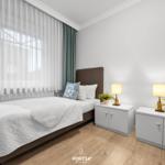 Schlafzimmer mit Bett, zwei Nachttischen und Fenster mit Vorhängen.