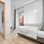 Schlafzimmer mit Bett, Fenster und Sicht auf Balkon. Holzboden und angrenzender Essbereich.