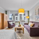 Wohnbereich mit Sofa, Sessel und TV. Große Fenster mit Blick auf Balkon.