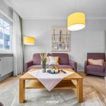 Wohnzimmer mit Sofa, Sessel und Tisch. Fenster, Wandbild und Bett sichtbar.