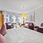 Schlafzimmer mit Doppelbett, Sitzgruppe und Balkonansicht.