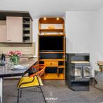 Küche mit Esstisch, TV-Schrank und Kaminofen. Blumen und Wein auf Tisch.