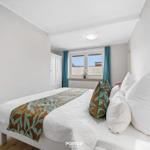 Schlafzimmer mit weißem Bett, blauen Vorhängen und Holzboden.