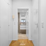 Flur mit Holzboden und Blick in das Badezimmer mit Waschbecken und Spiegel.