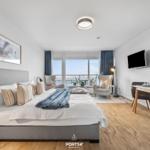 Schlafzimmer mit Bett, Sitzgelegenheiten und Blick auf Balkon. Esstisch mit Stühlen und Fernseher.