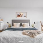 Schlafzimmer mit Bett, Nachttischen, Schrank und Sessel. Wandbild und Vorhänge sind sichtbar.