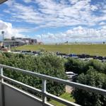 Blick vom Balkon auf Parkplatz, Grünfläche und Strand mit Wolkenhimmel.