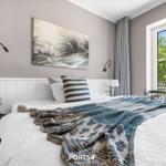Schlafzimmer mit Bett, Fenster und Wandbild. Blick auf grüne Bäume.
