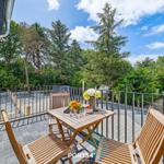 Terrasse mit Holztisch und Stühlen, Blick auf grüne Bäume und einen klaren Himmel.