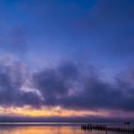 Sonnenuntergang über dem Wasser mit einem Pier und einem Boot.